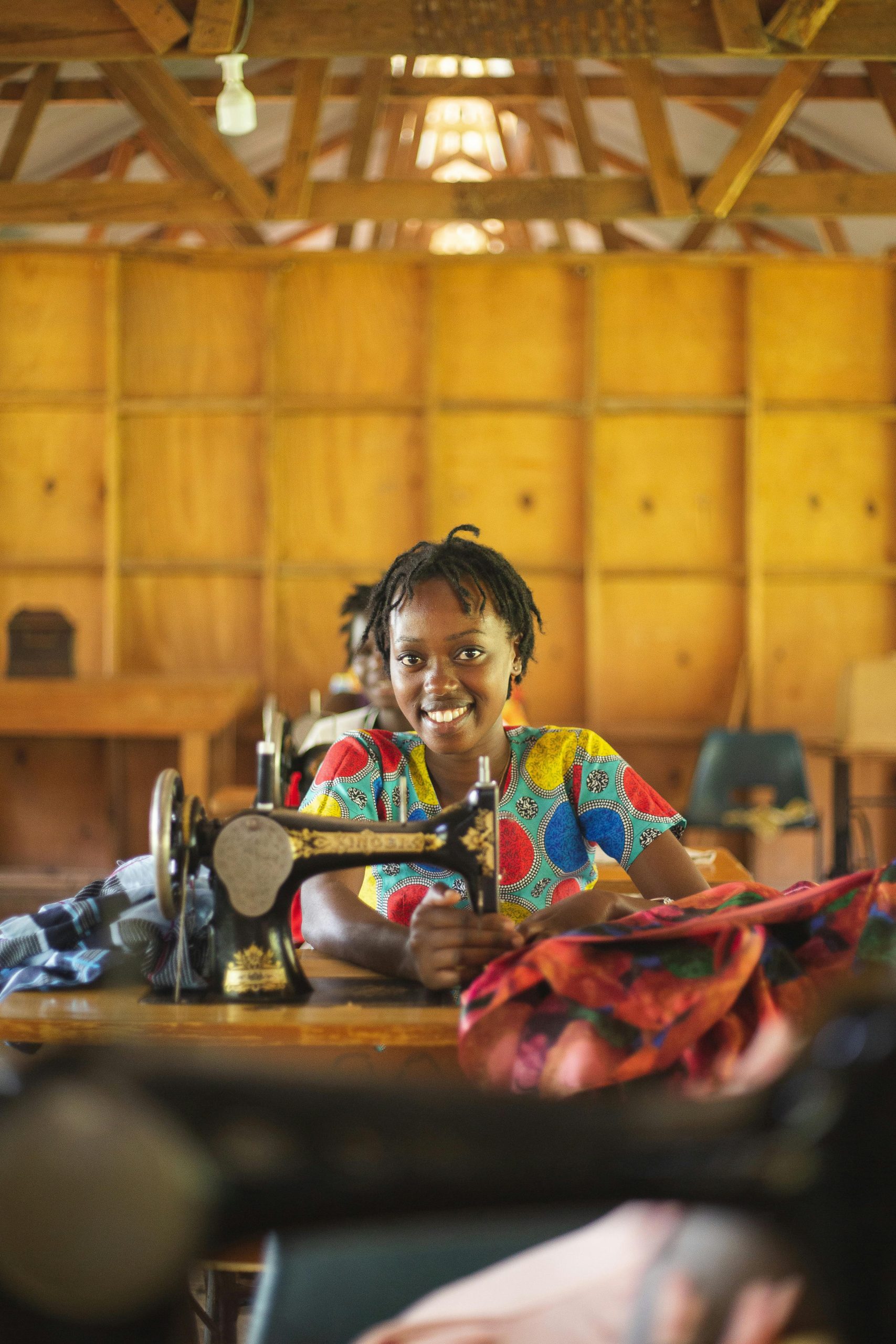 A young woman sewing with a smile in a vibrant workshop in Uganda.