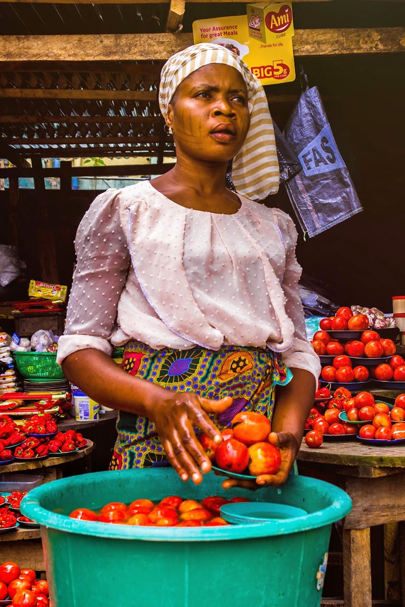 Woman selling fresh tomatoes at an outdoor market stall, showcasing vibrant produce.